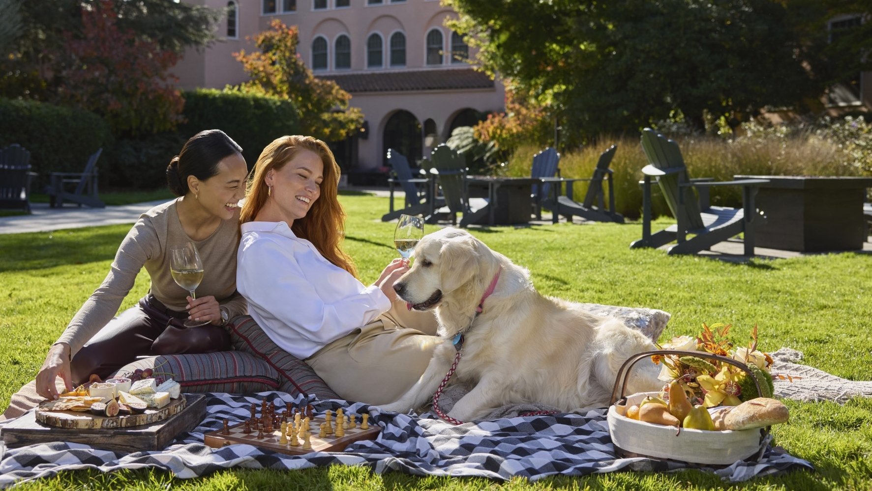 two women enjoying a picnic on the lawn with a golden retriever dog